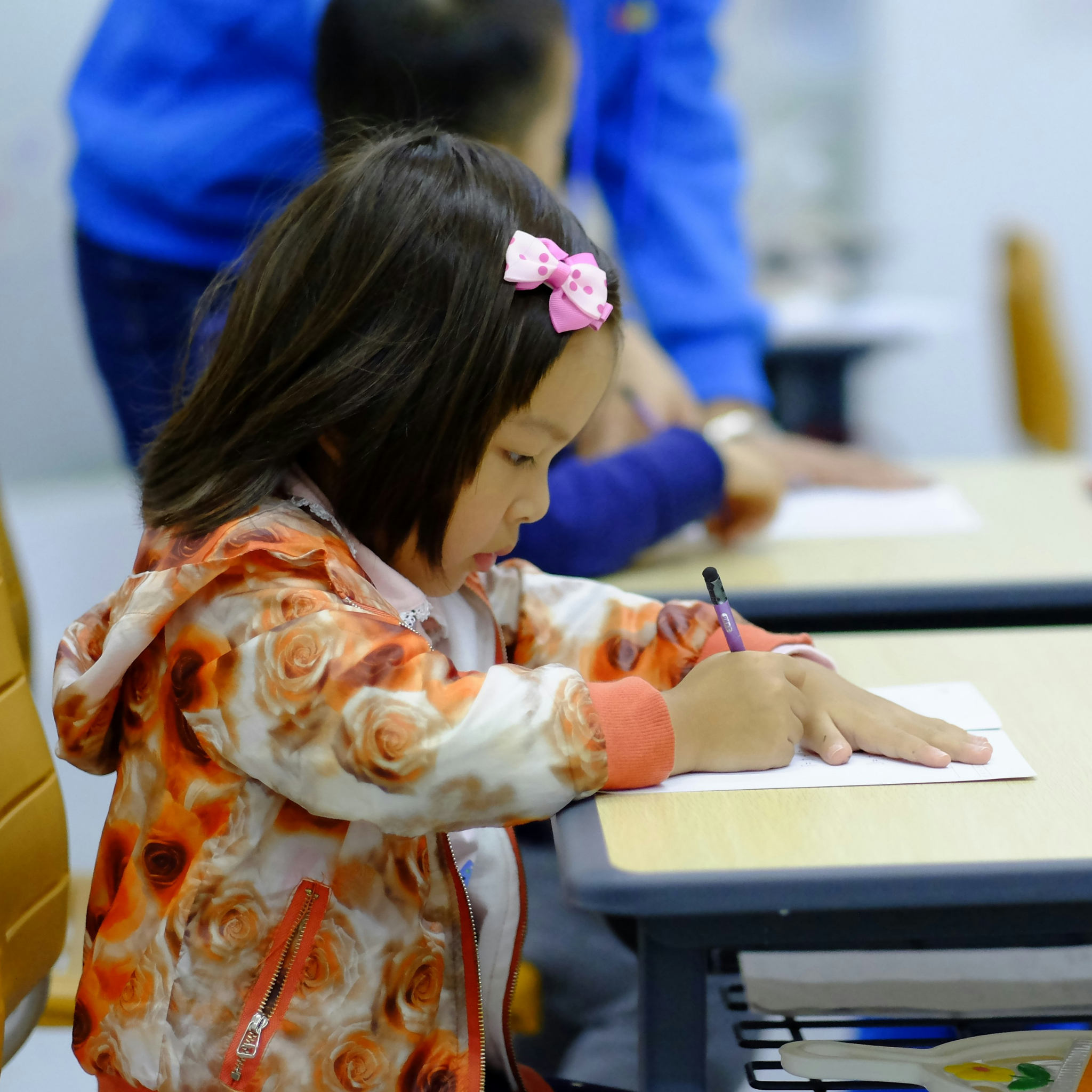 Child writing at a desk in a classroom setting